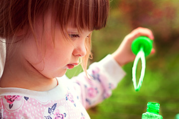Little girl with bangs concentrated trying to blow soap bubbles