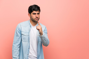 Young man over pink wall frustrated and pointing to the front