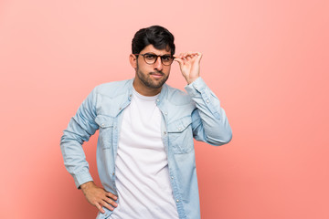 Young man over pink wall with glasses and surprised