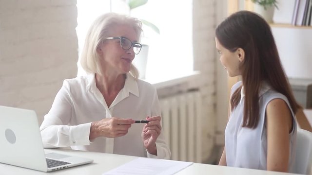 Happy young client handshaking trusted old broker signing contract