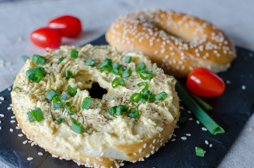Bagel with hummus, spices, green onion, tomatoes cherry and sesame seeds on the black stone desk. Close up.