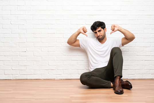 Young man sitting on the floor showing thumb down