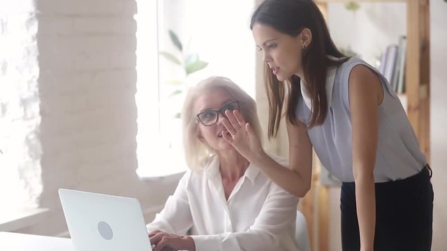 Young mentor manager helping old worker explaining computer work instructing