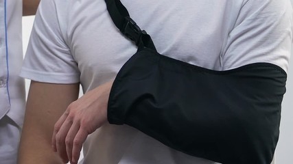 Doctor applying male patient arm sling, treatment after trauma, car accident