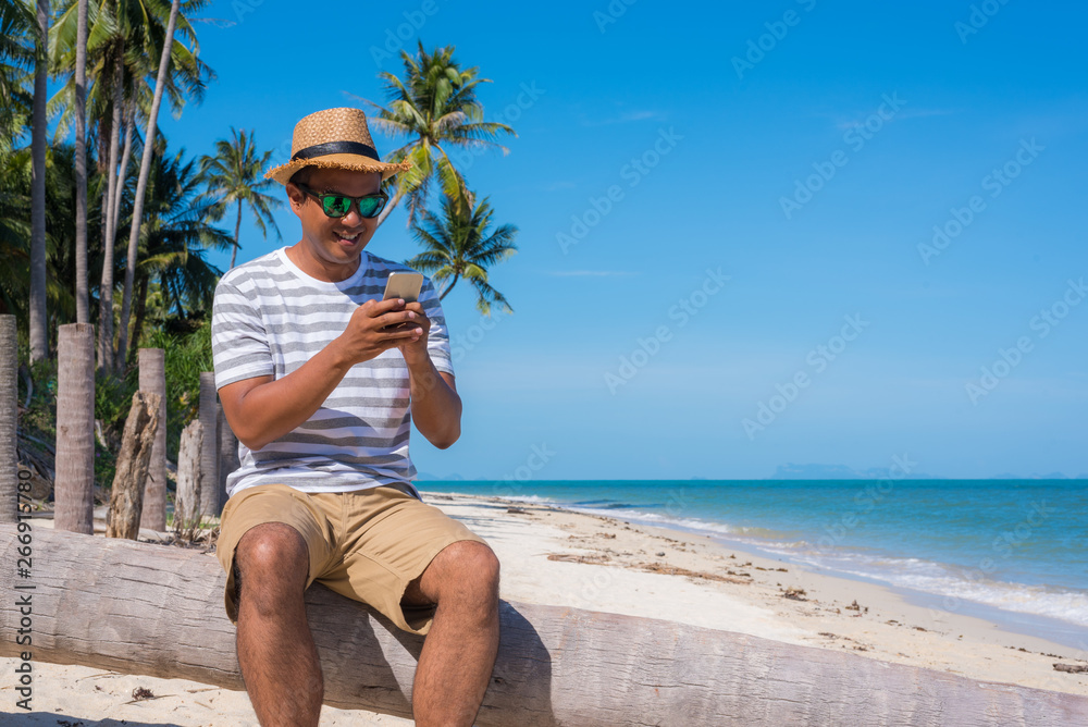 Wall mural young asian man on the beach using smartphone.