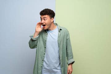 Young man over blue and green background shouting with mouth wide open to the lateral