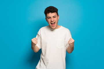 Young man over blue background celebrating a victory in winner position