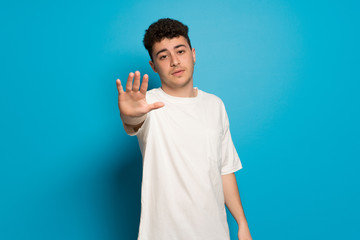 Young man over blue background making stop gesture denying a situation that thinks wrong