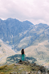 Fototapeta na wymiar Rear view of a young woman standing on a mountain in Kazbegi, Georgia. Wanderlust travel concept