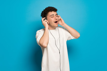 Young man over blue background listening to music with headphones