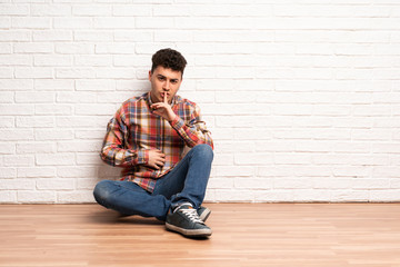Young man sitting on the floor showing a sign of silence gesture putting finger in mouth