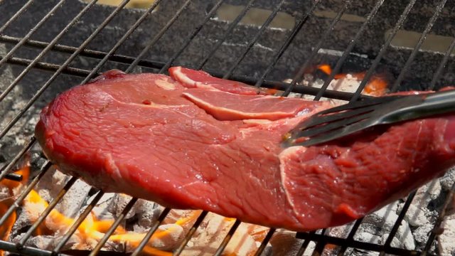 Chef puts steak using metal tongs on the grill grate
