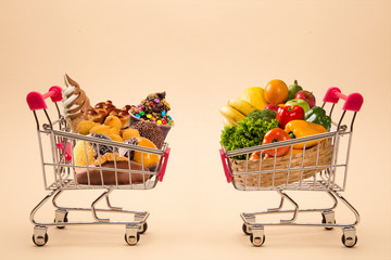 Concept of food and diet. Wafers, chocolate, ice cream and fruits and vegetables in shopping cart. Fast food addiction. Struggling with overweight and obesity. comparison between light food and fatten