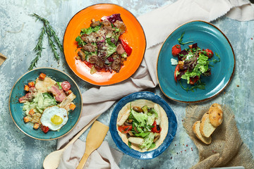 Multi-colored plates with different salads. Beautiful serving of dishes. Light gray background. Restaurant menu