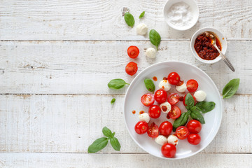Colorful ingredients of Caprese salad on a white wooden table with a copy space, flat lay style
