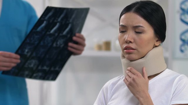 Sad female patient feeling uncomfortable in cervical collar, doctor examination