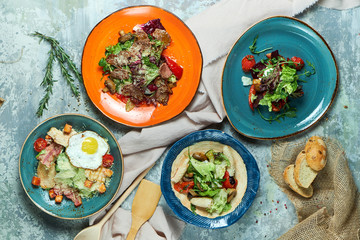 Multi-colored plates with different salads. Beautiful serving of dishes. Light gray background. Restaurant menu