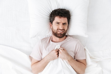 Displeased young man in the morning under blanket in bed.