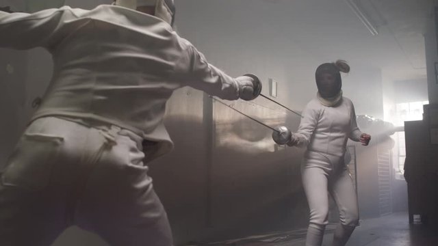 Push-in on a female fencer parry and riposte in a dark and dingy fencing gym in slow motion