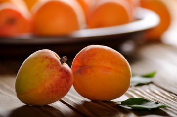 Clay dish full of ripe apricots on wooden table