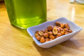 Salted fried peanuts in a plate near green beer on a table