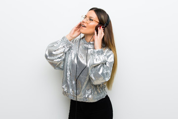 Young woman with glasses over white wall listening to music with headphones