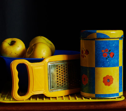 Ingredients for some vegetarian meal with apples; a graper, a tin and a blue bowl with fresh ripe yellow apples on black background, close-up, copy space