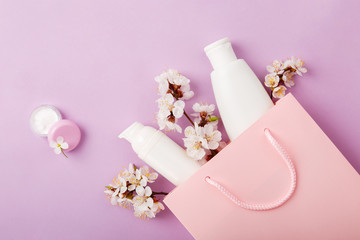 Set of woman's cosmetics in a bag with spring apricot bloom. Women's secrets. Spring female skin and hair care cosmetics in a bag on purple background. Cosmetic with apricot. Shampoo, lotion, tonic