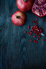 Healthy fresh pomegranates on a dark wooden background. A spoon with grains of fresh pomegranate. Vibrant focus. Dark wooden background. View from above.