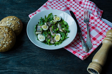 Marinated herring with arugula, onions, boiled quail eggs and lemon juice and olive oil. Delicious salad. Proper nutrition. Dark wooden background.