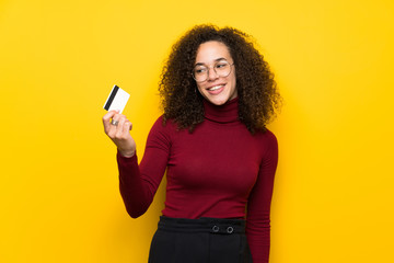 Dominican woman with turtleneck sweater holding a credit card and thinking