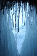 view from  ice cave. frozen, crystal clear water drops like stalactites hang from the ceiling. rising sun stained ice. partially tinted photo. focus on a central object. Extra shallow depth of field.