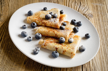 a plate of pancakes with blueberries and sugar powder on wooden background