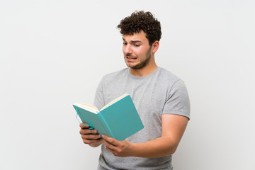 Man with curly hair over isolated wall holding and reading a book