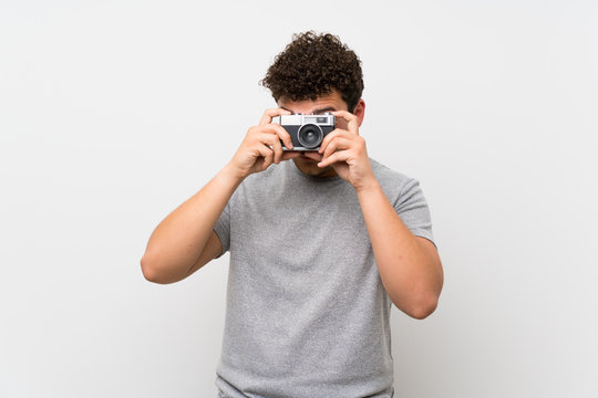 Man with curly hair over isolated wall holding a camera