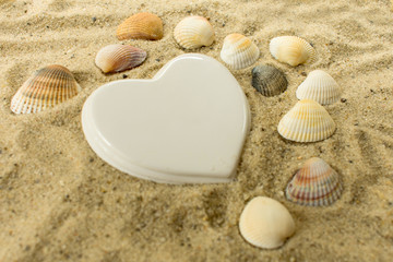  white porcelain heart and shells in the sand on the beach.