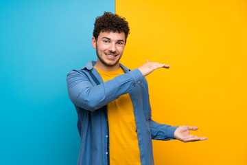 Man with curly hair over colorful wall holding copyspace to insert an ad