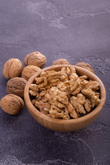 Cracked and whole walnuts in wooden bowl and on blue slate surface. Healthy nuts and seeds composition.