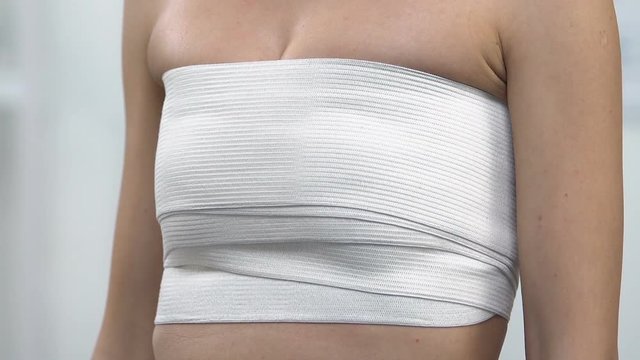 Female patient touching breast in chest compression wrap, lifting surgery