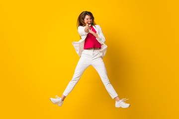 Young woman jumping over isolated yellow wall pointing to the front