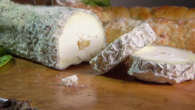 Fork lifts a piece of cheese. Goat cheese with blue-grey mould has a long straw that traverses the middle.
