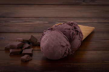 chocolate ice cream scoops in waffle cones and chocolate pieces on wooden background