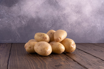 Heap of fresh clean potatoes on rustic wooden surface and slate textured background. Organic food,...
