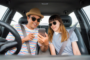 Couple asian man and woman sitting in car and looking at smartphone. Travel concept.