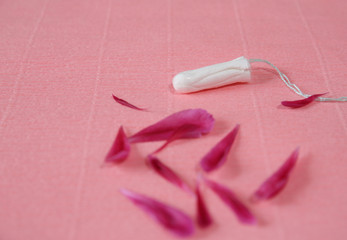 Clean white cotton tampon with red peony petals on pink background. Copy space. Menstruation. Feminine Hygiene in periods, beauty treatment.
