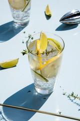 Lemonade or mojito cocktail with lemon and lime, cold refreshing drink or beverage with ice on a light blue backround. Retro style with artistic trendy shadows.