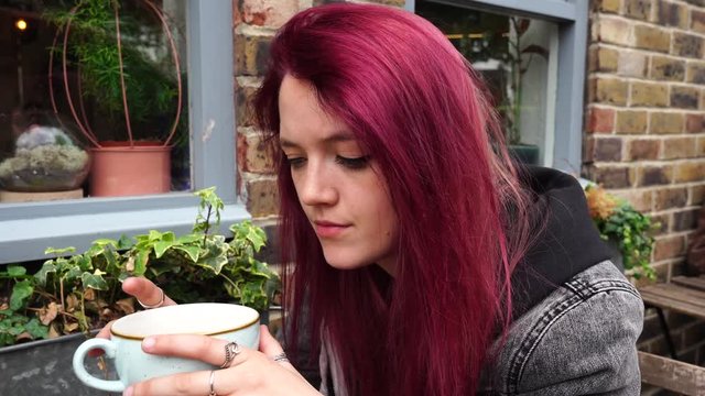 Emo girl drinking tea outside a cafe and looking at camera, slightly annoyed