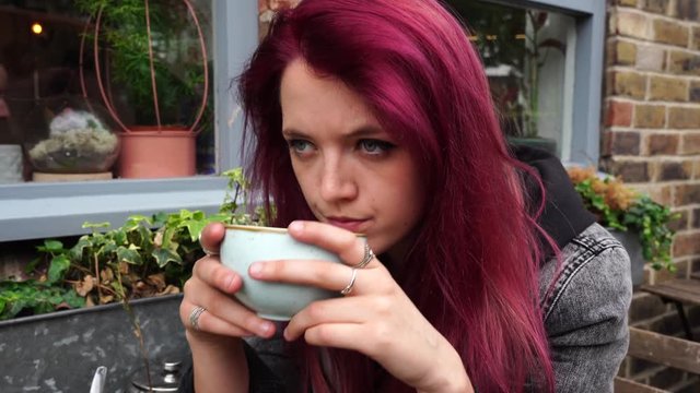 Emo girl drinking tea outside a cafe and looking at camera, slightly annoyed