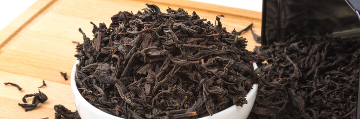 Dried tea is poured into a ceramic cup on a wooden board on a white background.