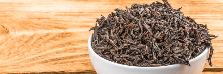 Dried tea is poured into a ceramic cup on a wooden plank table.